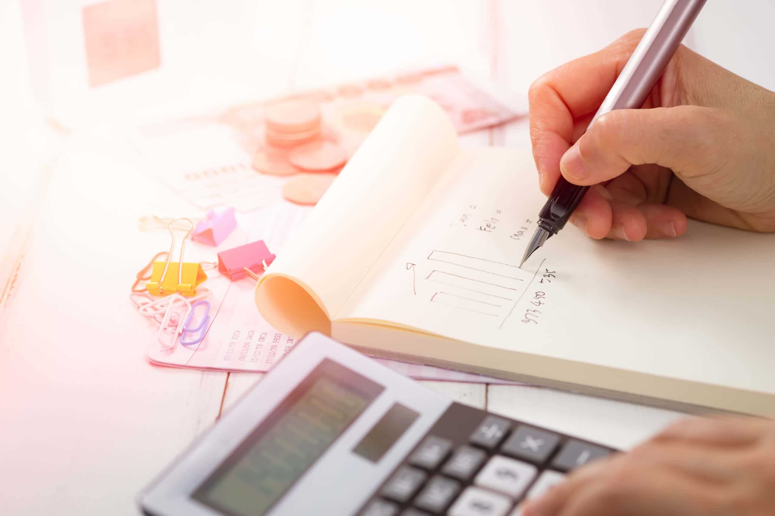 a person writing in a notebook next to a calculator