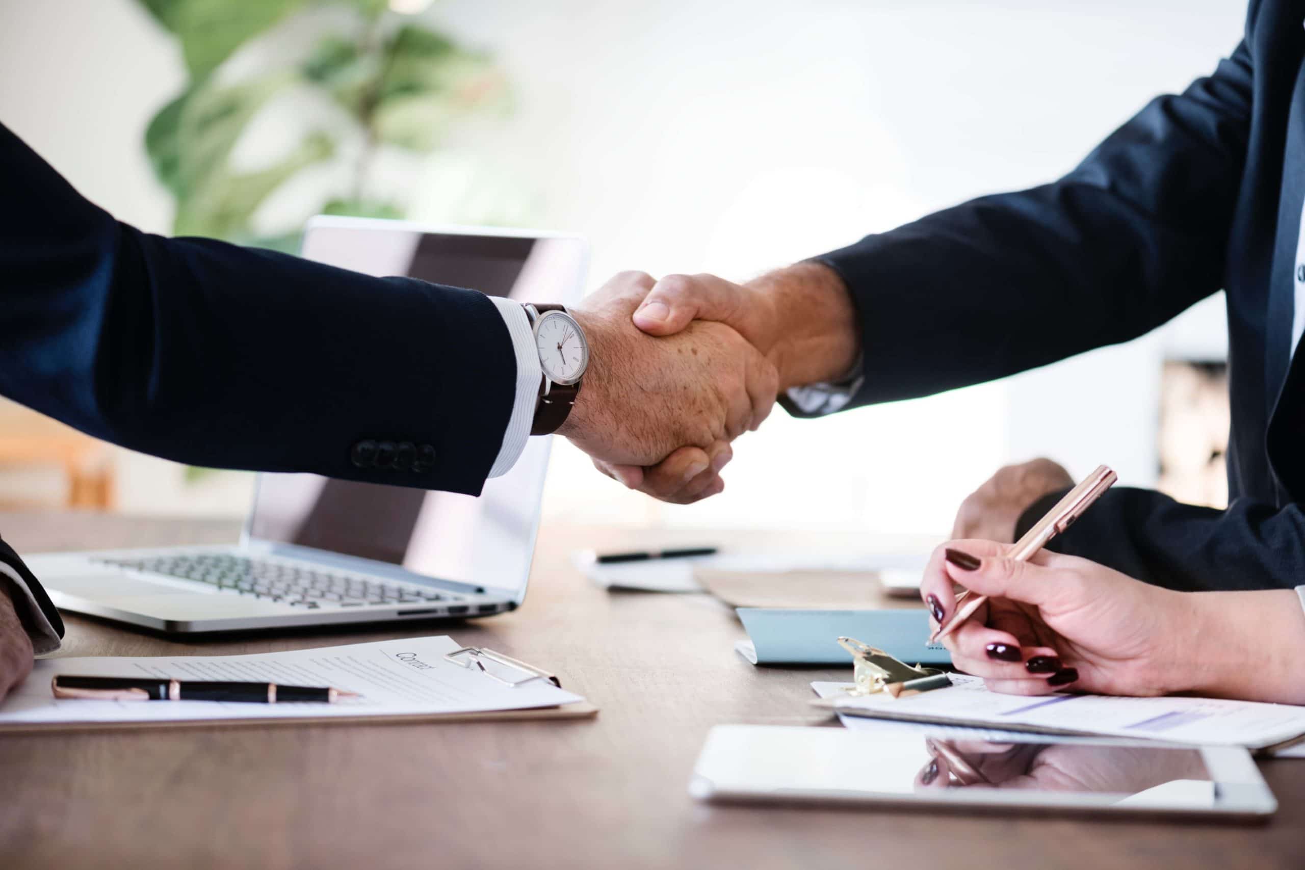 a man in a suit shakes hands with man while a woman signs a document