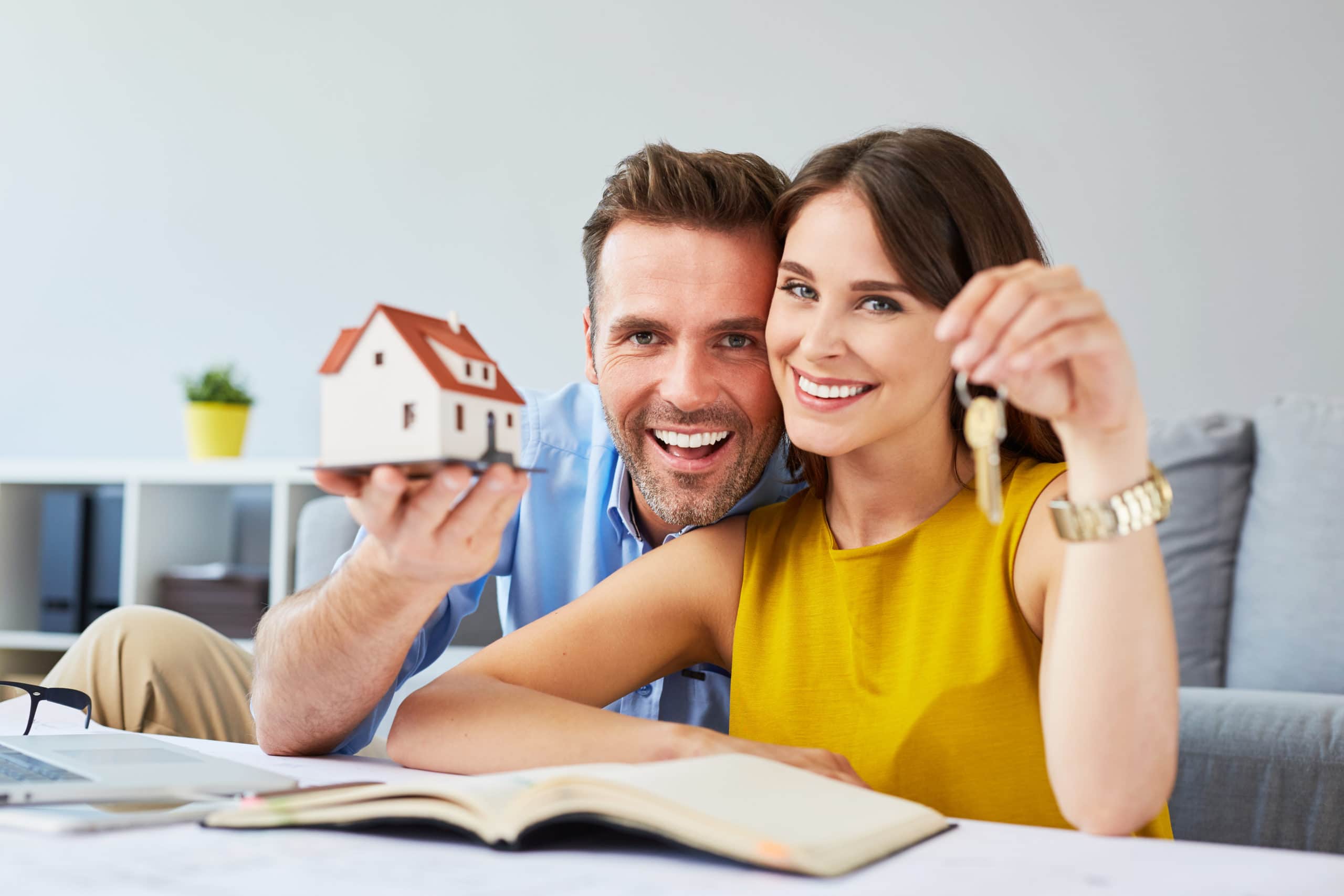 Happy couple holding keys to new home and house miniature