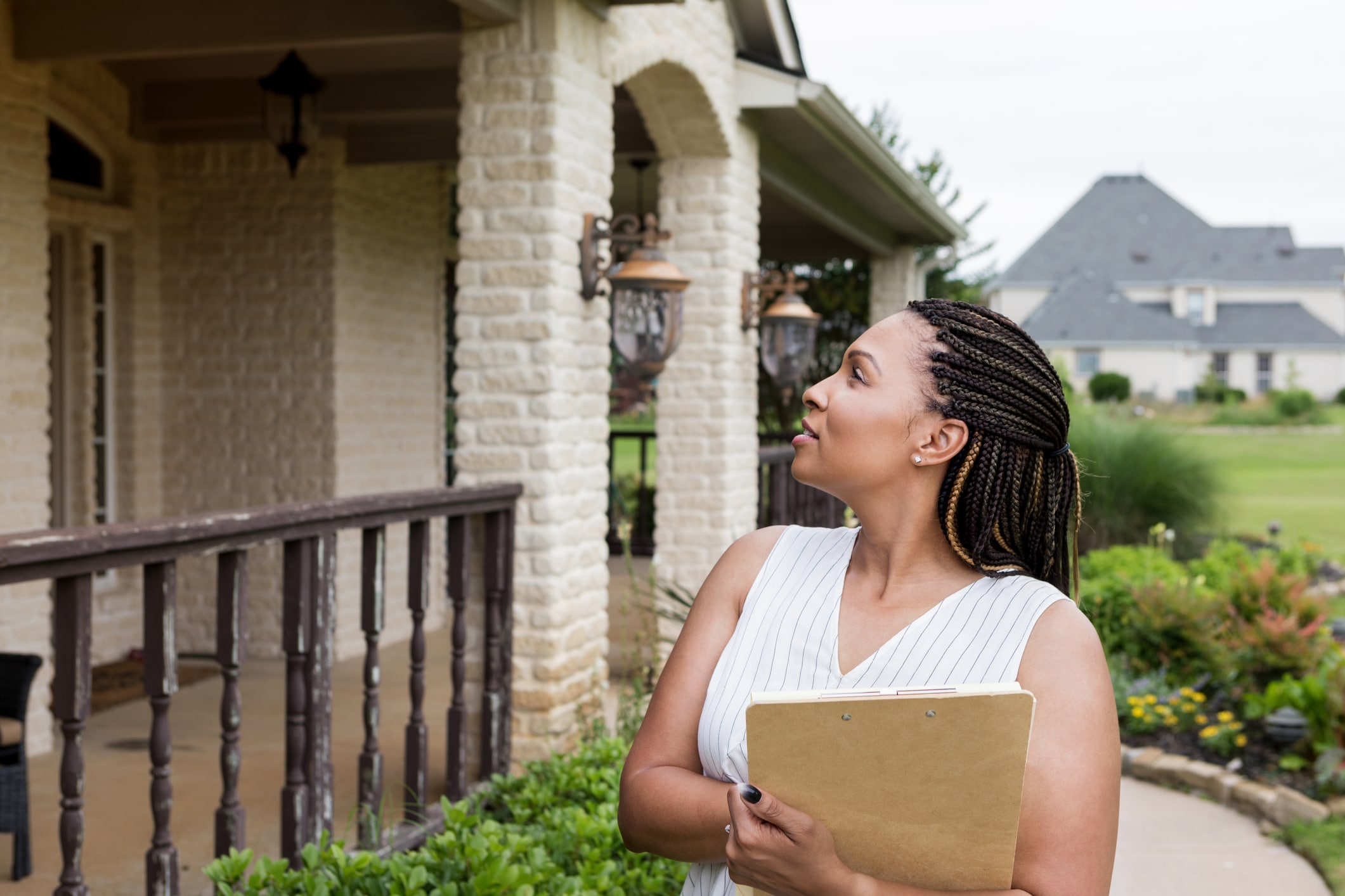 a woman holding a clipboard stands in front of a house