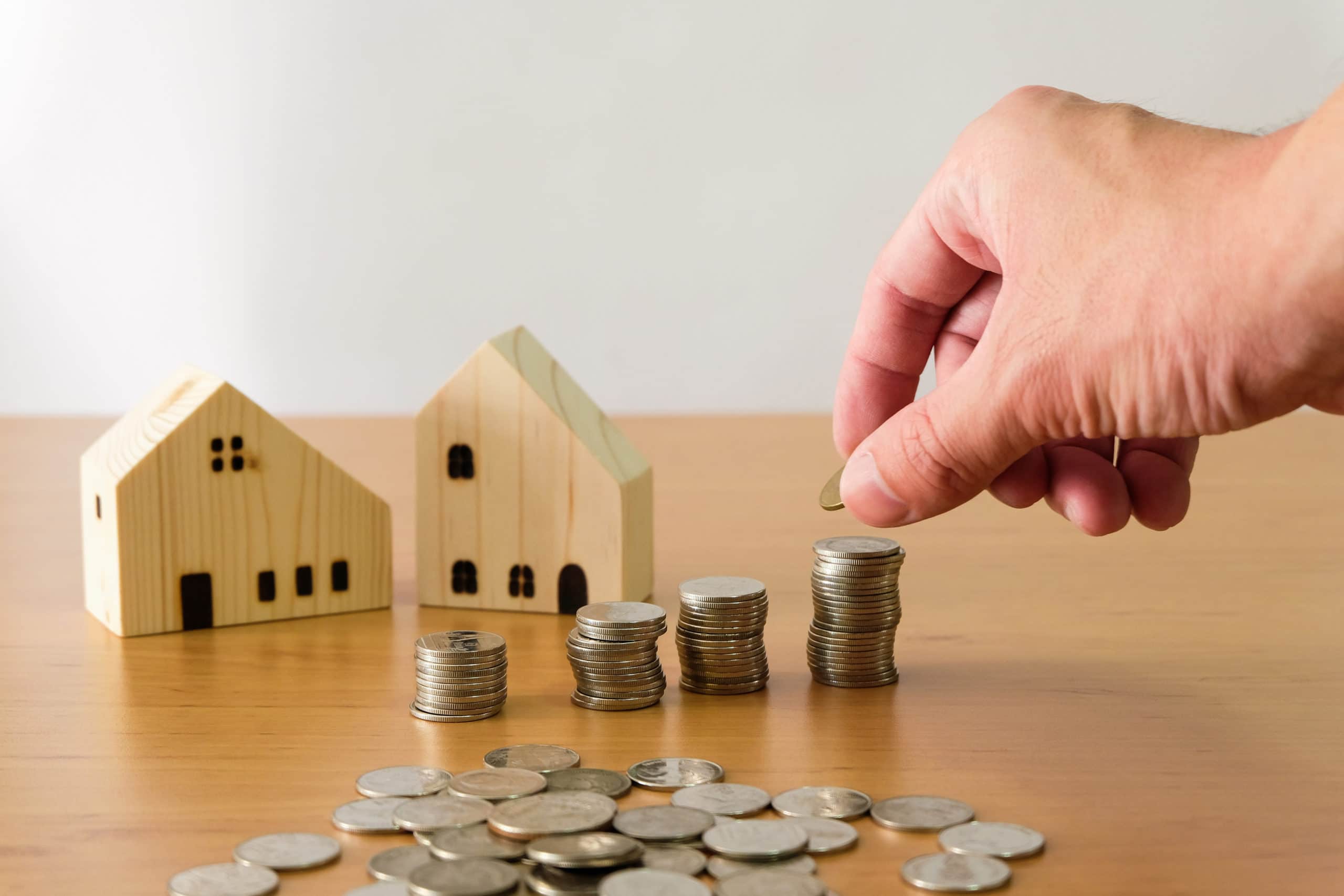 Selective focus Men hand puting coin on stack of money coin for saving for home, property with small wood house on the background. Wealth and saving plan for house mortgage Personal investment concept