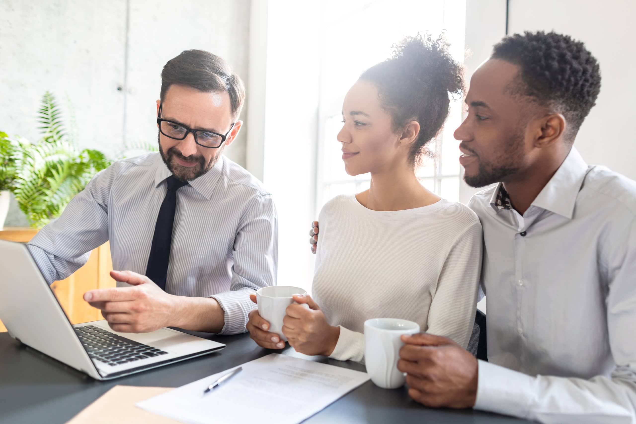 a man and woman sit at a table looking at a laptop with a mortgage lender