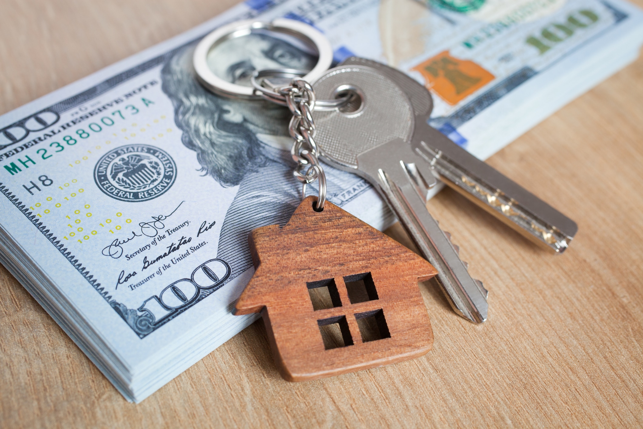 a house keychain sitting on top of a stack of 100 dollar bills