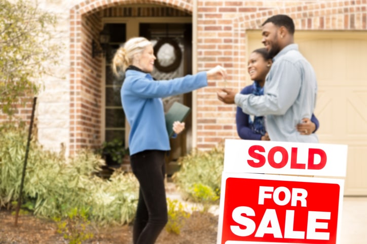 a couple standing in front of a sold for sale sign