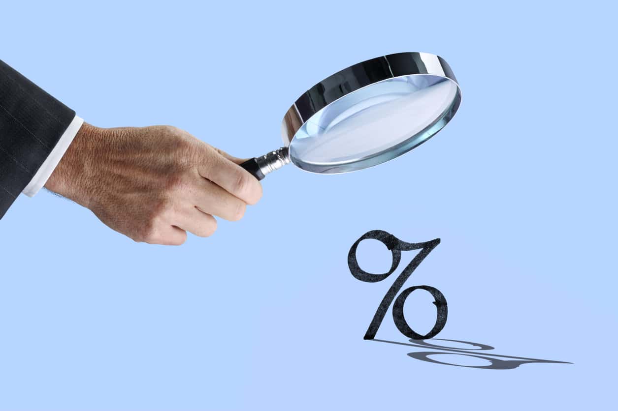 a hand holding a magnifying glass over a percentage symbol