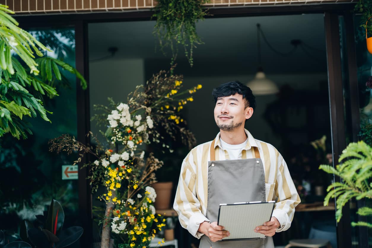 a man in an apron holding a clipboard in front of a green exit sign